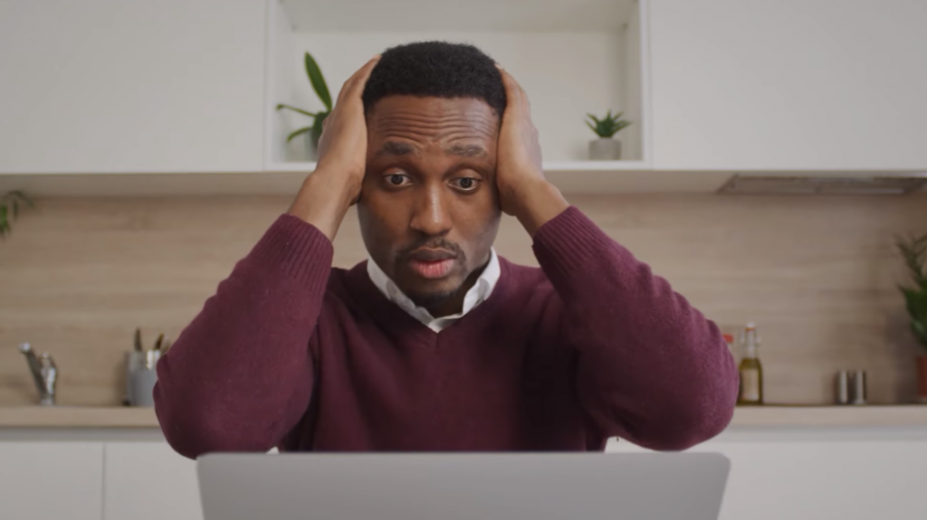 colored man sitting in front of his computer with shocked gesture and hands on his head