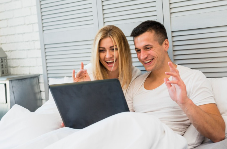 young smiling couple with laptop and blanket on bed
