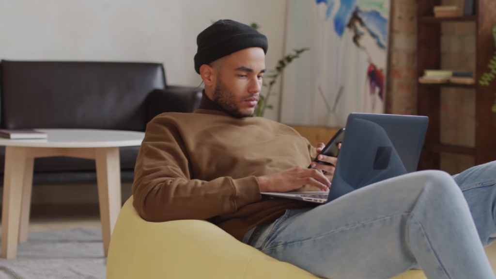 Man sitting on the couch checking his cell phone and laptop
