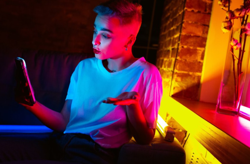 stylish woman in neon lighted interior. bright neoned colors. caucasian model using smartphone in colorful lights indoors. 