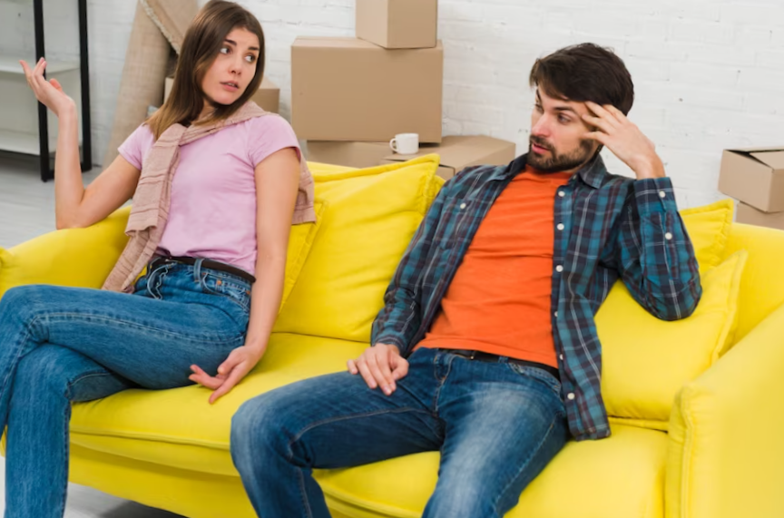 two upset young couple sitting on yellow sofa in their new house
